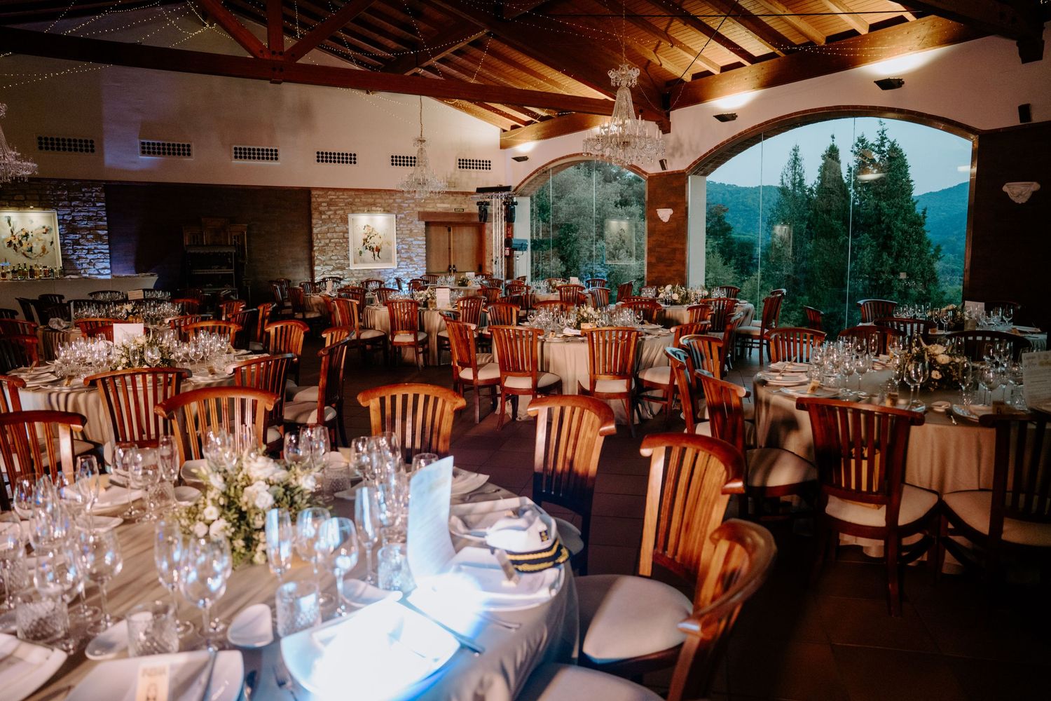 Elegant wedding reception venue with wooden chairs and tables set for dinner under exposed beam ceiling.