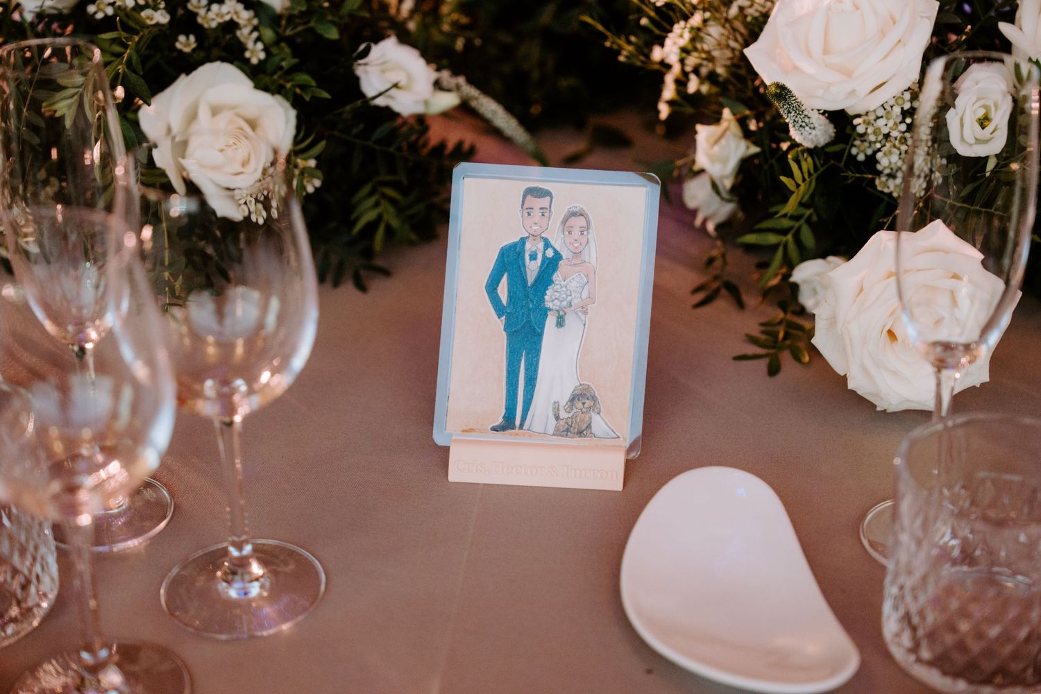 Elegant wedding reception table settings with white roses, greenery, and crystal glassware.