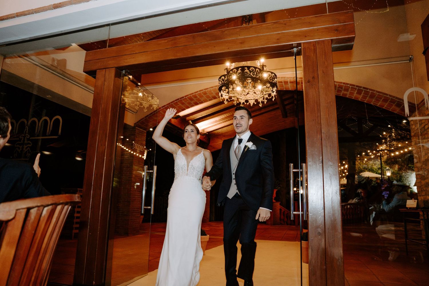 Wedding guests dancing and celebrating on a wooden dance floor under elegant chandeliers at an indoor reception venue.