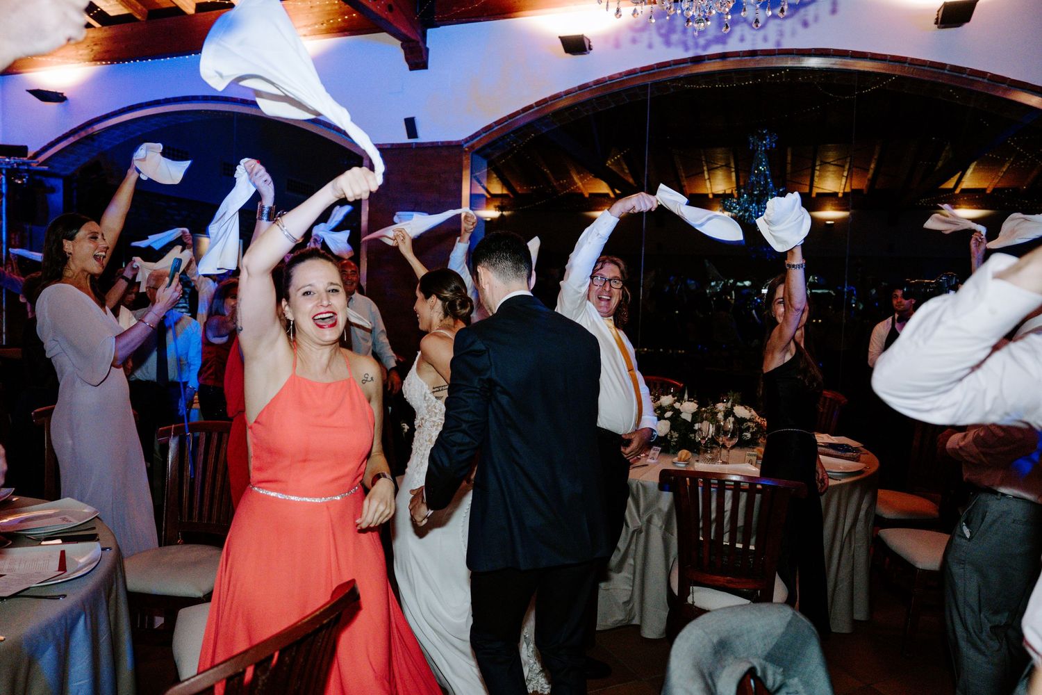 Wedding celebration with guests dancing and having fun under blue and purple lighting effects.