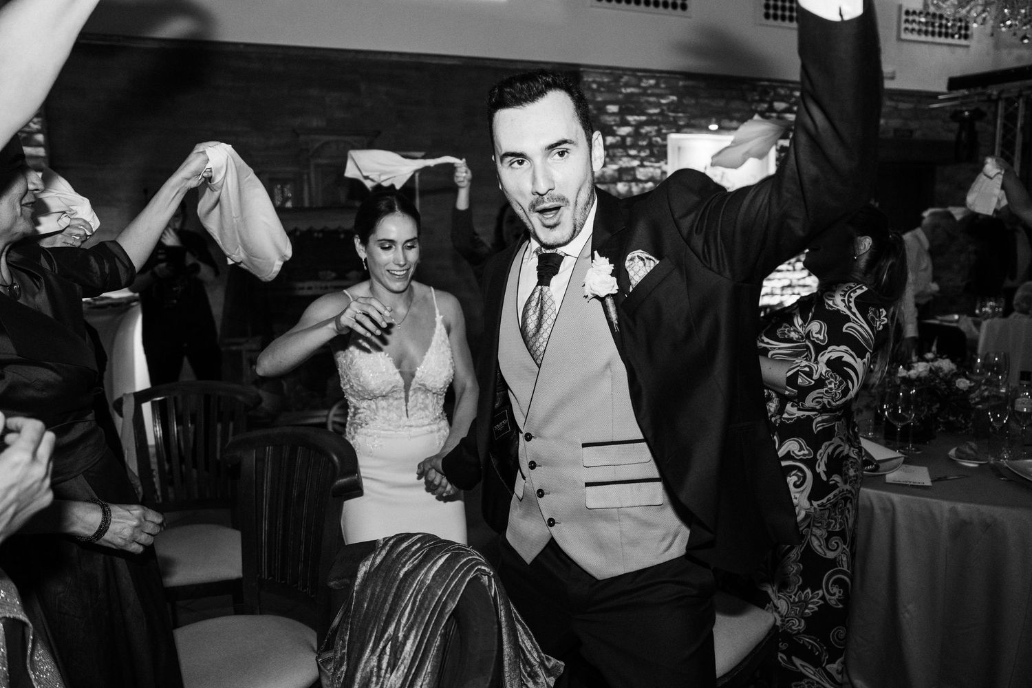 Black and white photo of wedding guests dancing and laughing at a lively reception party.