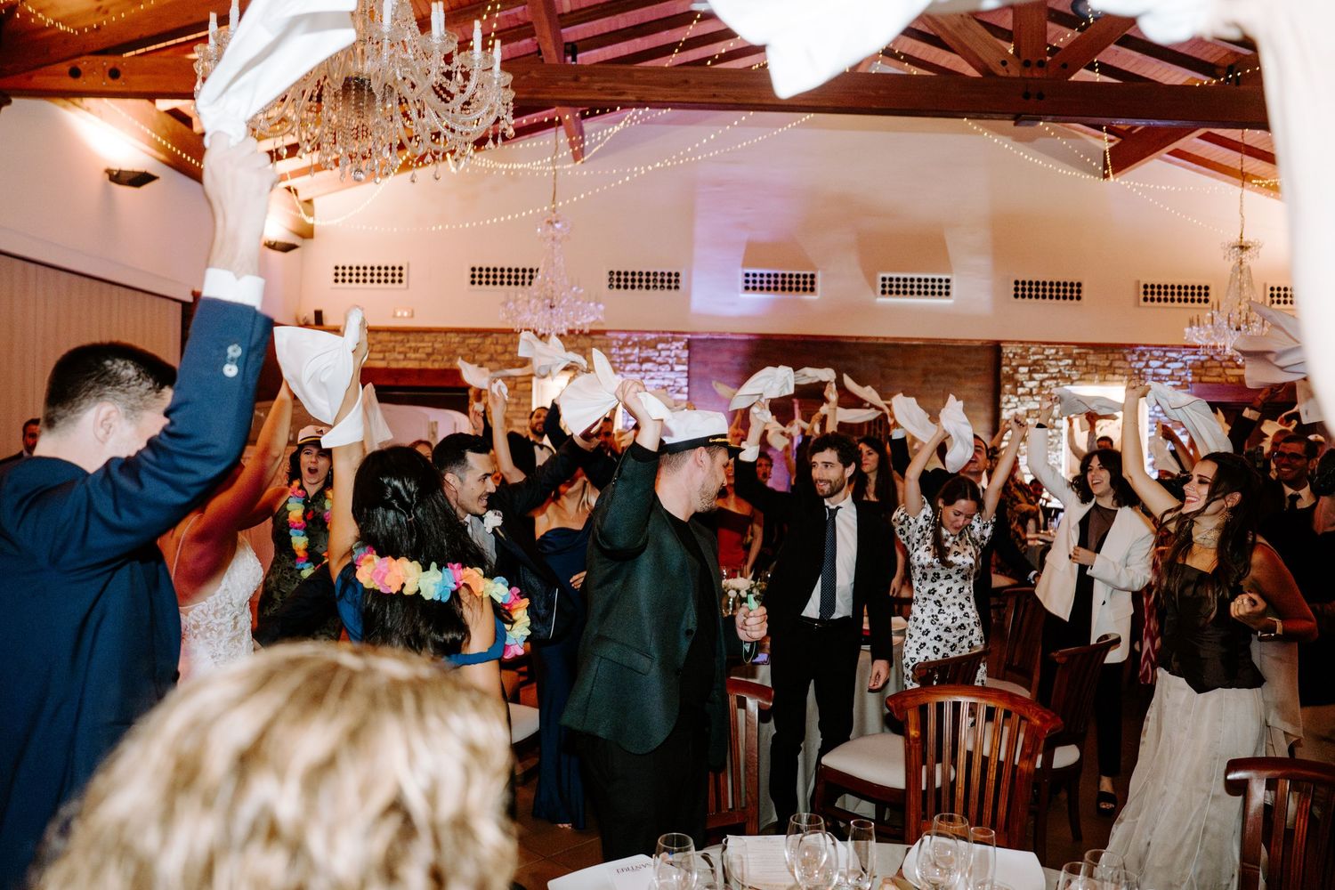Wedding reception venue with exposed wooden beams and elegant lighting during an energetic dance party.