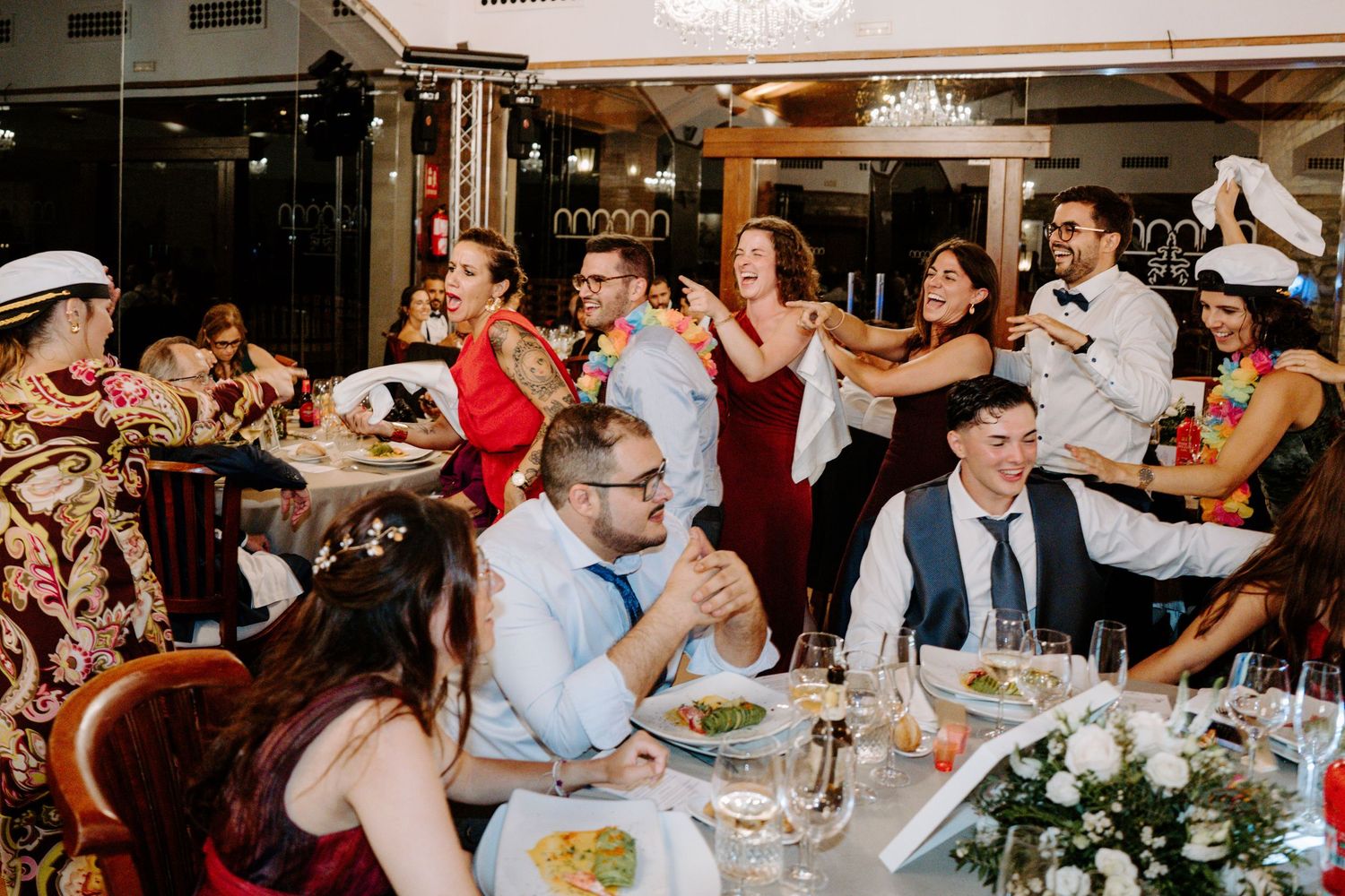 Wedding guests dancing and celebrating at tables during a reception in an elegant indoor venue.