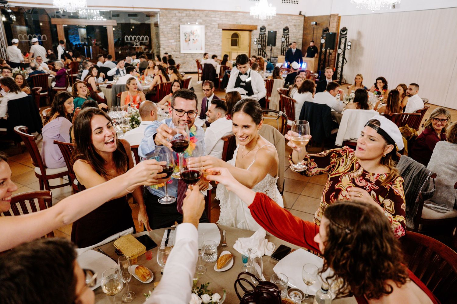 Wide view of a wedding reception hall filled with guests at round tables during celebrations.