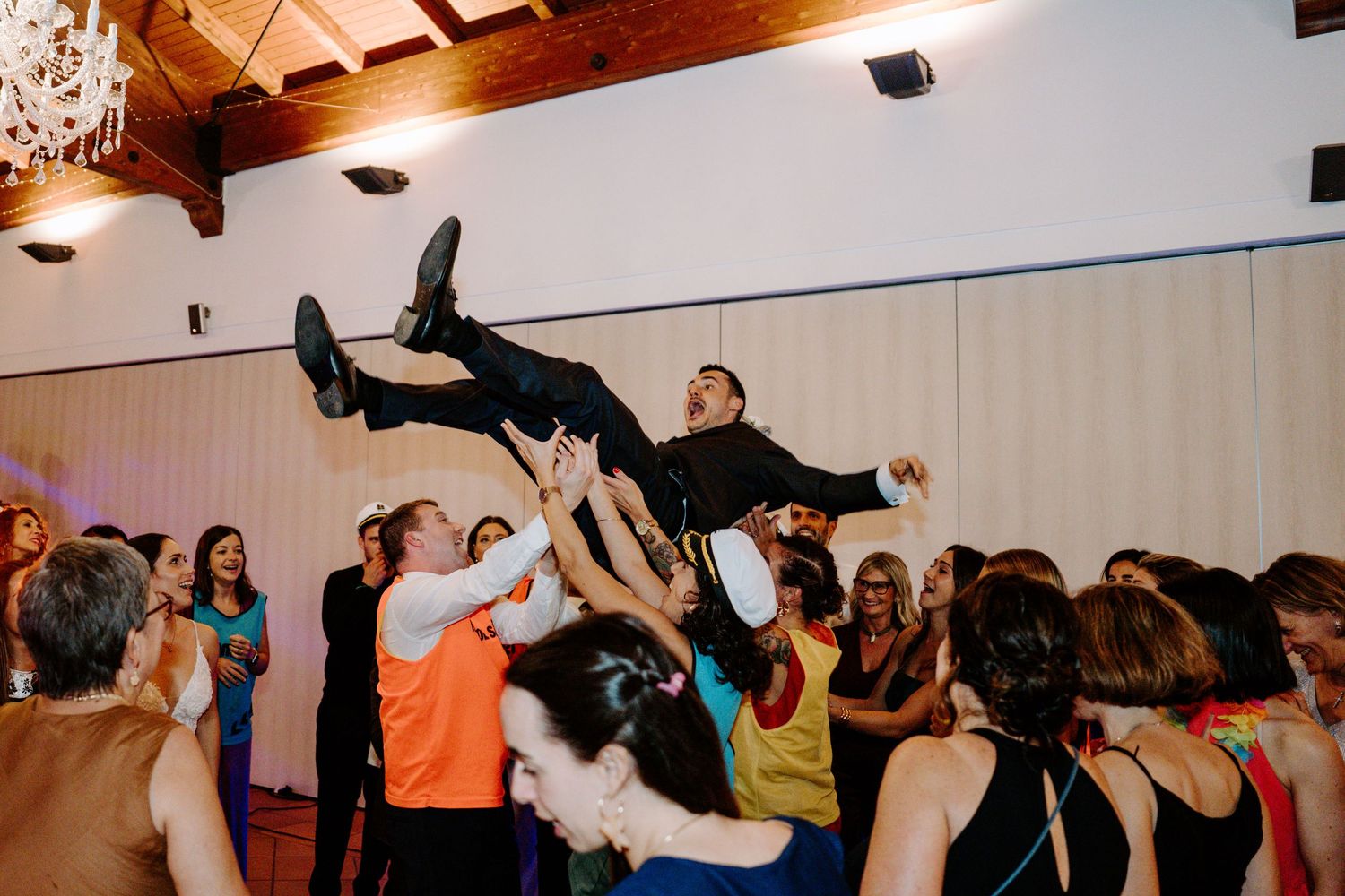 Dynamic shot of wedding guests dancing with raised arms at reception party.