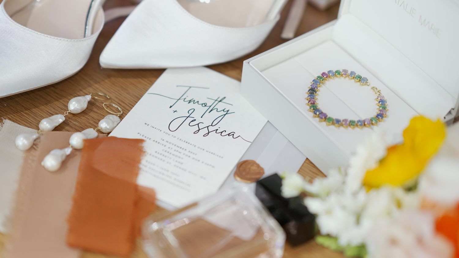 Wedding accessories including white shoes, invitation card and delicate jewelry on wooden surface.