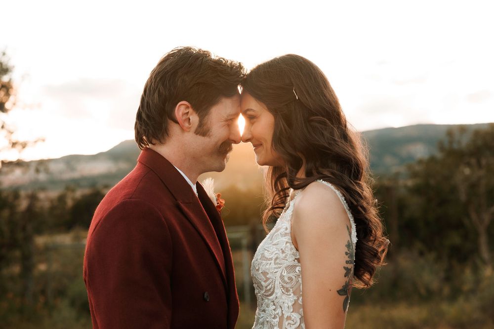 Bride and groom share an intimate forehead-touch moment at golden sunset in a scenic outdoor landscape.