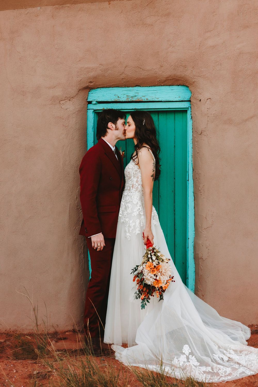 Wedding couple shares a kiss in front of a rustic turquoise door on a adobe building in the Southwest.