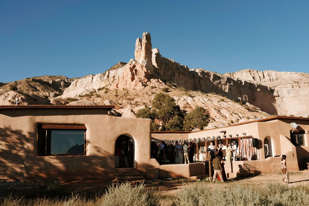 Wedding guests gather outside a Southwestern adobe venue beneath dramatic sandstone spire rock formations.
