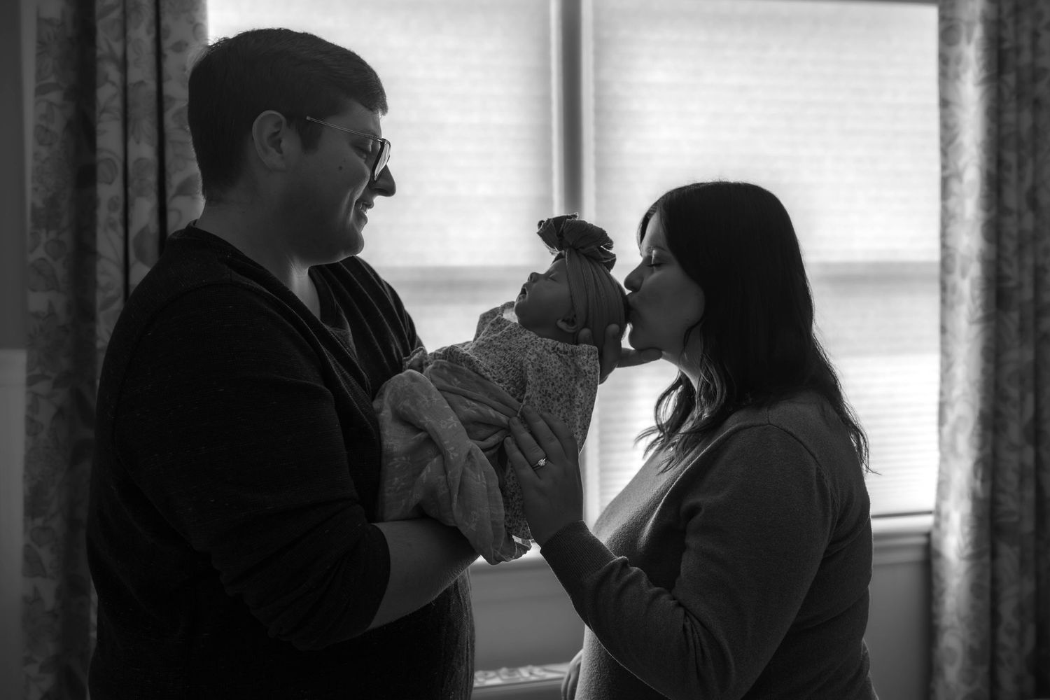 A black and white photo shows people gathered in a hallway with windows, creating a candid social scene.