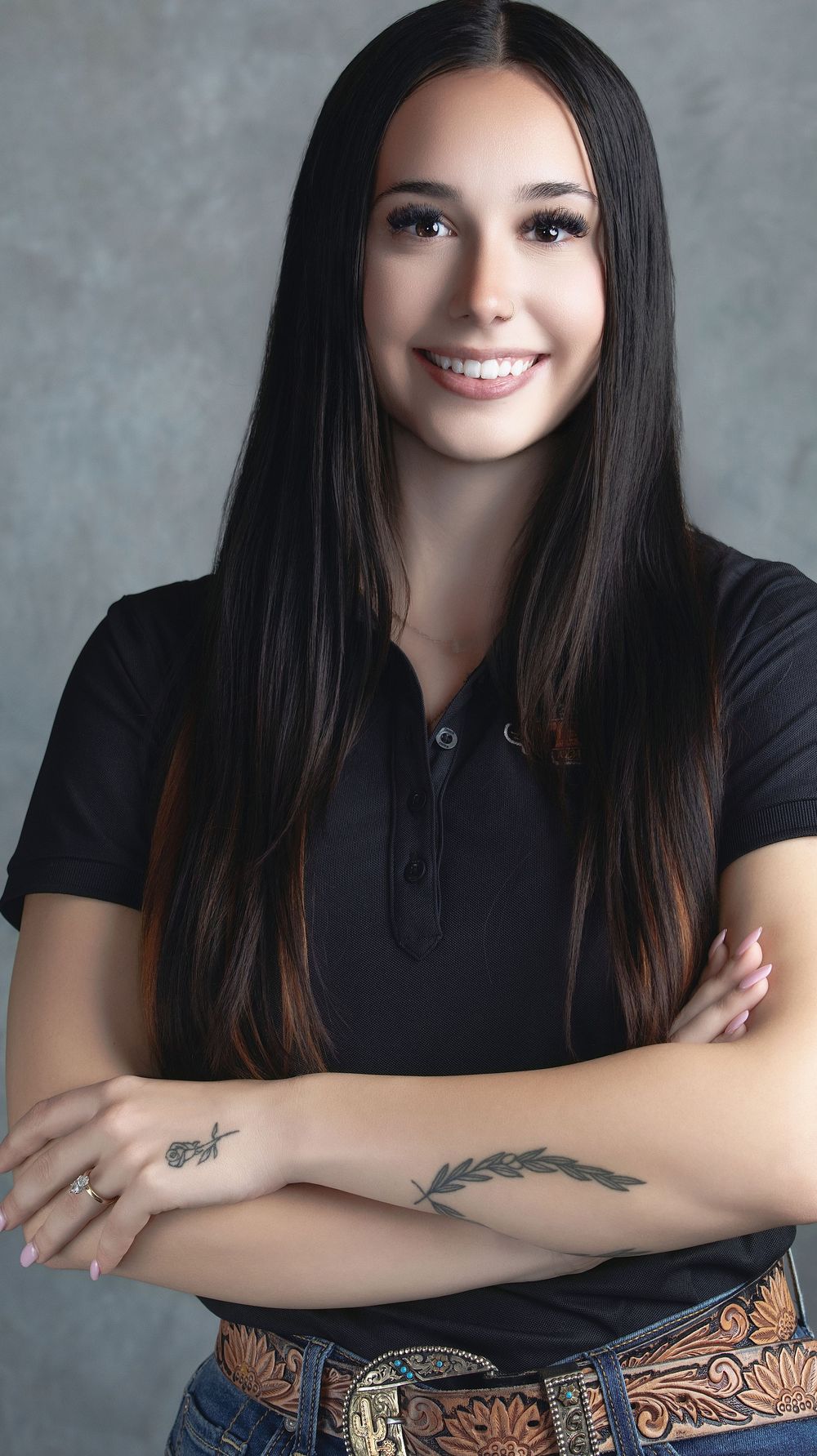 Studio portrait with black shirt and decorative leather belt against grey background.
