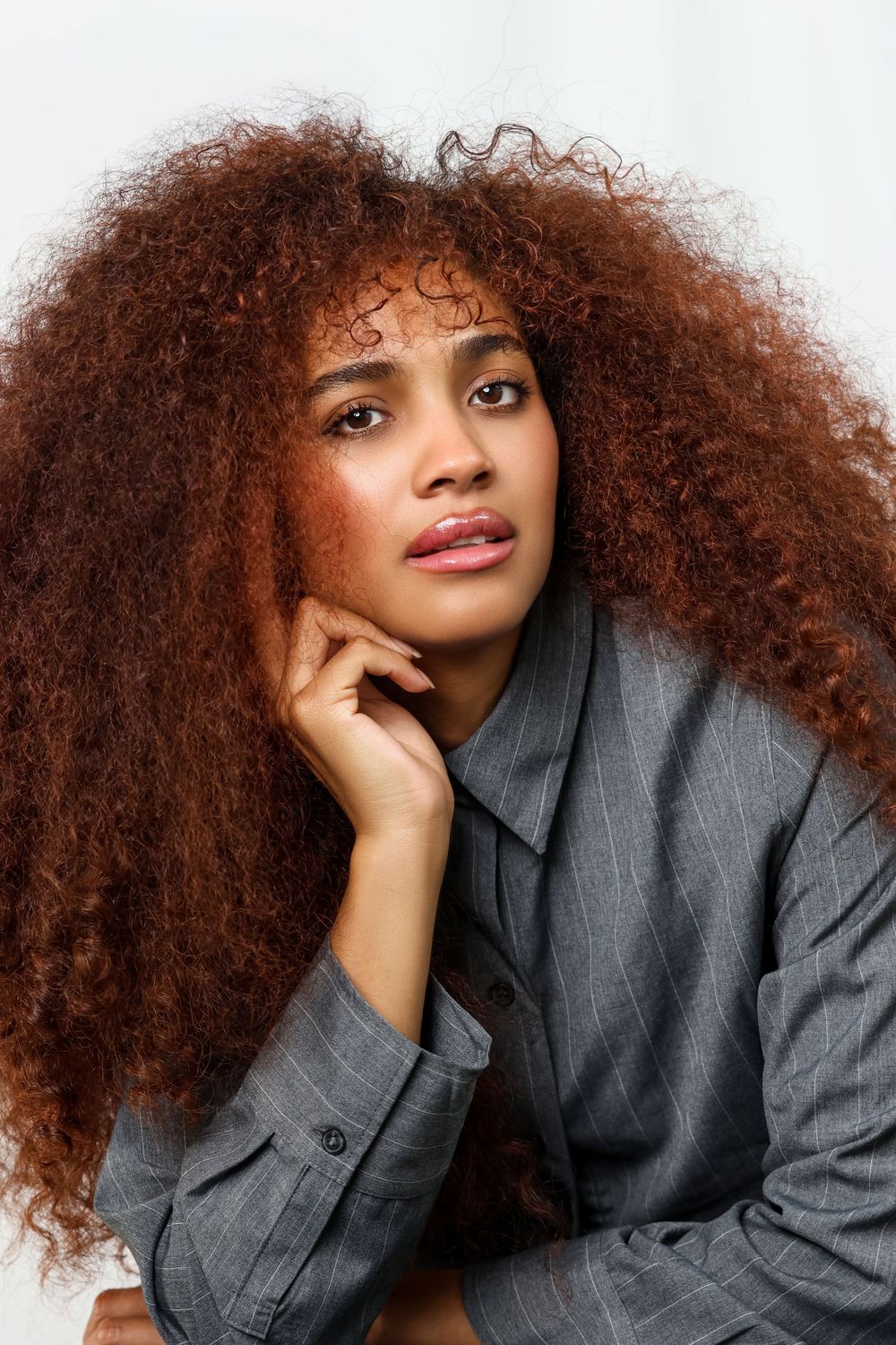 Fashion portrait with voluminous curly hair and grey blazer against neutral background.