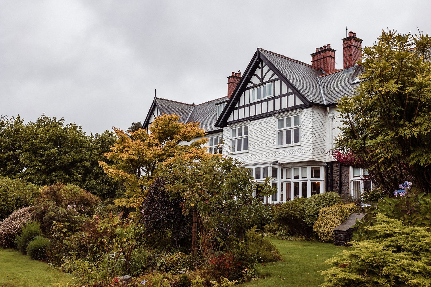 Elegant white Tudor-style home with gabled roofs and traditional architectural details nestled among lush greenery.