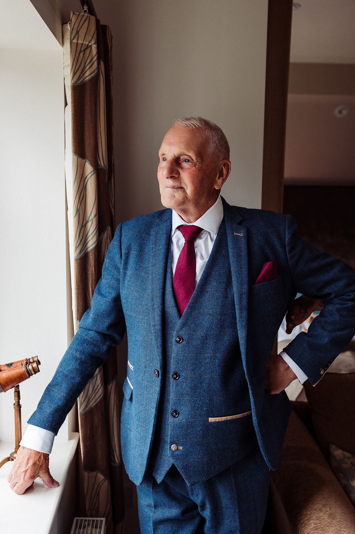 A person wearing a tailored blue three-piece suit with a burgundy tie poses in multiple elegant stances.