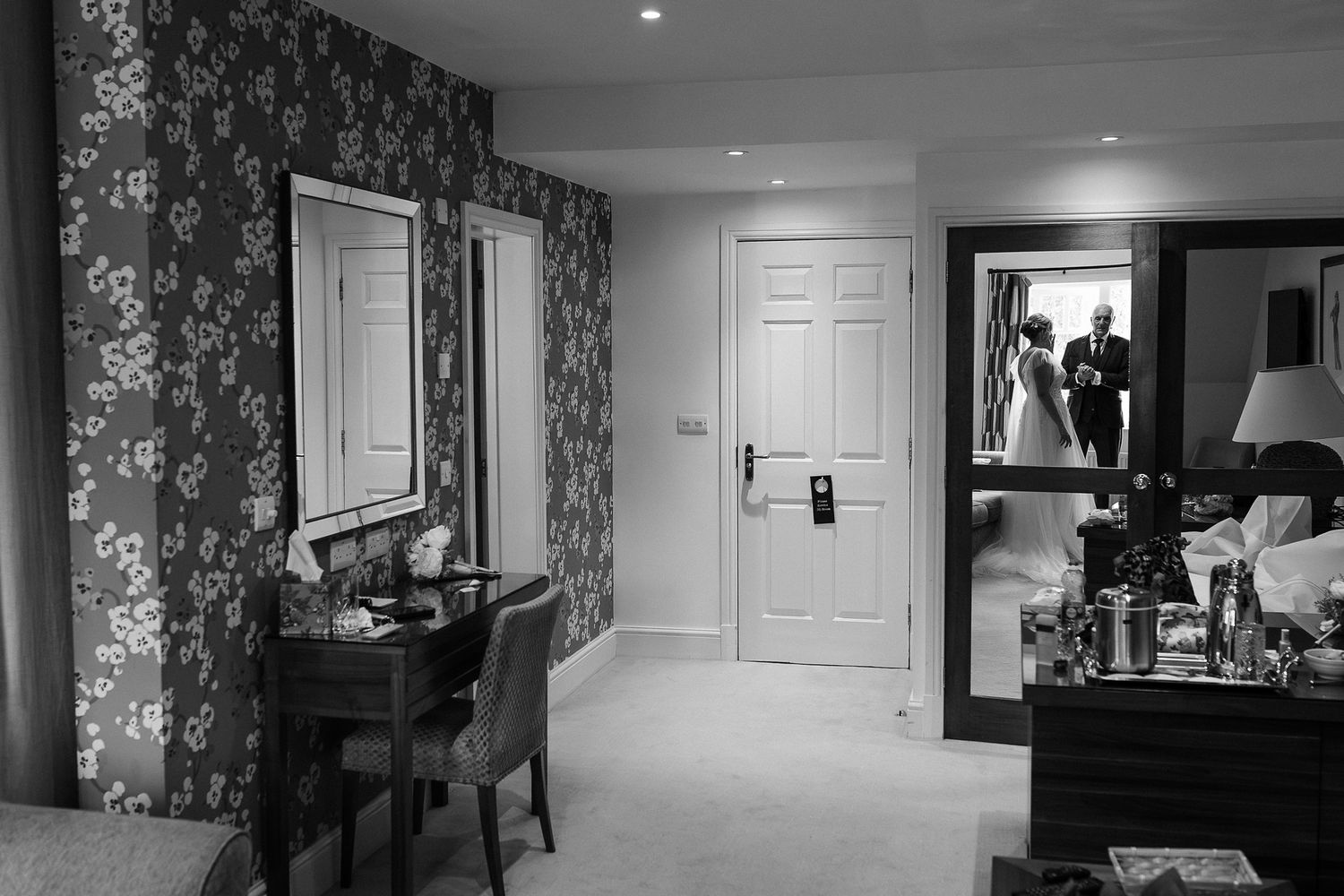 Elegant hallway with white doors and ornate wallpaper features recessed lighting and dark wood furniture.