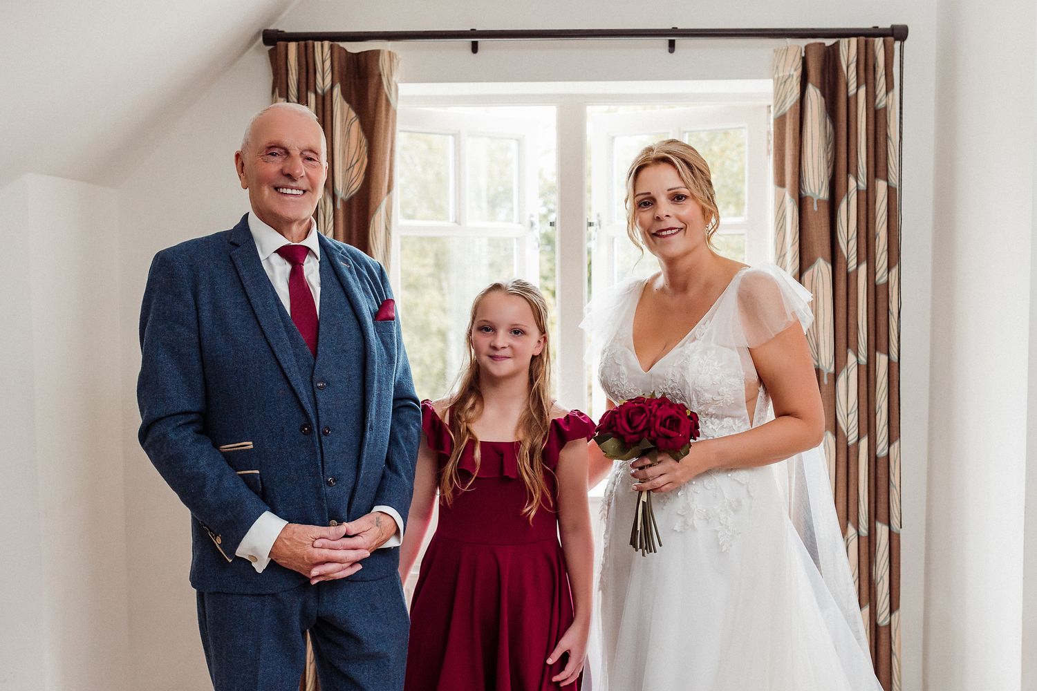 Wedding party poses in elegant indoor setting with burgundy and white color scheme.