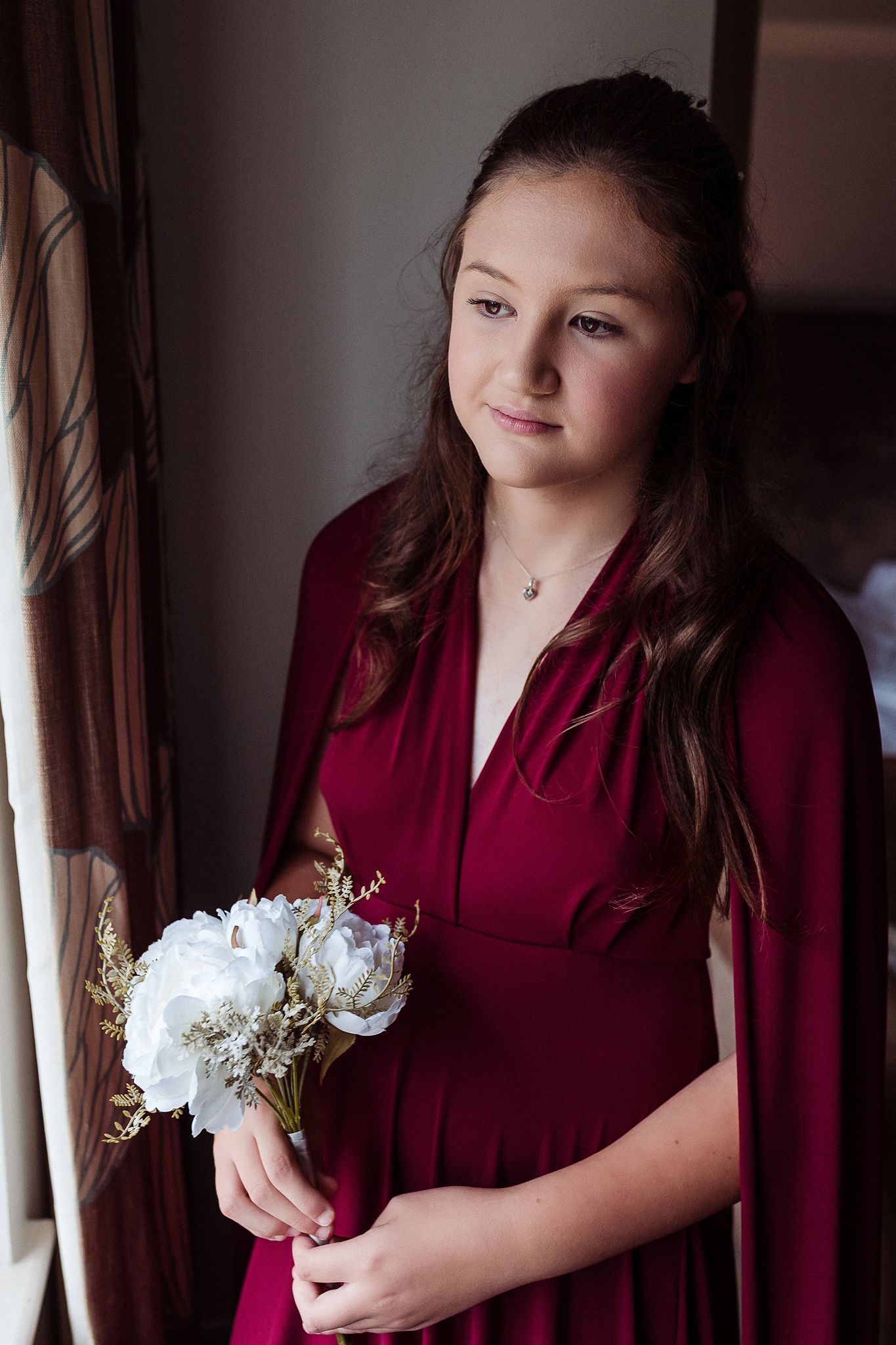 A series of moody portraits showing someone in a burgundy top holding delicate white flowers against a dark background.