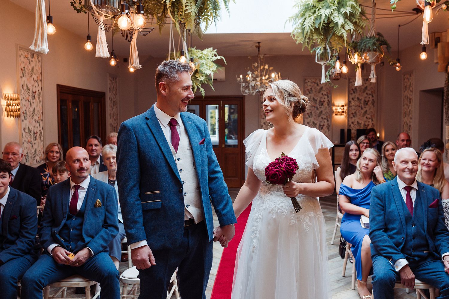 A wedding party in blue suits and a bride in white gather for celebration photos at an indoor venue.
