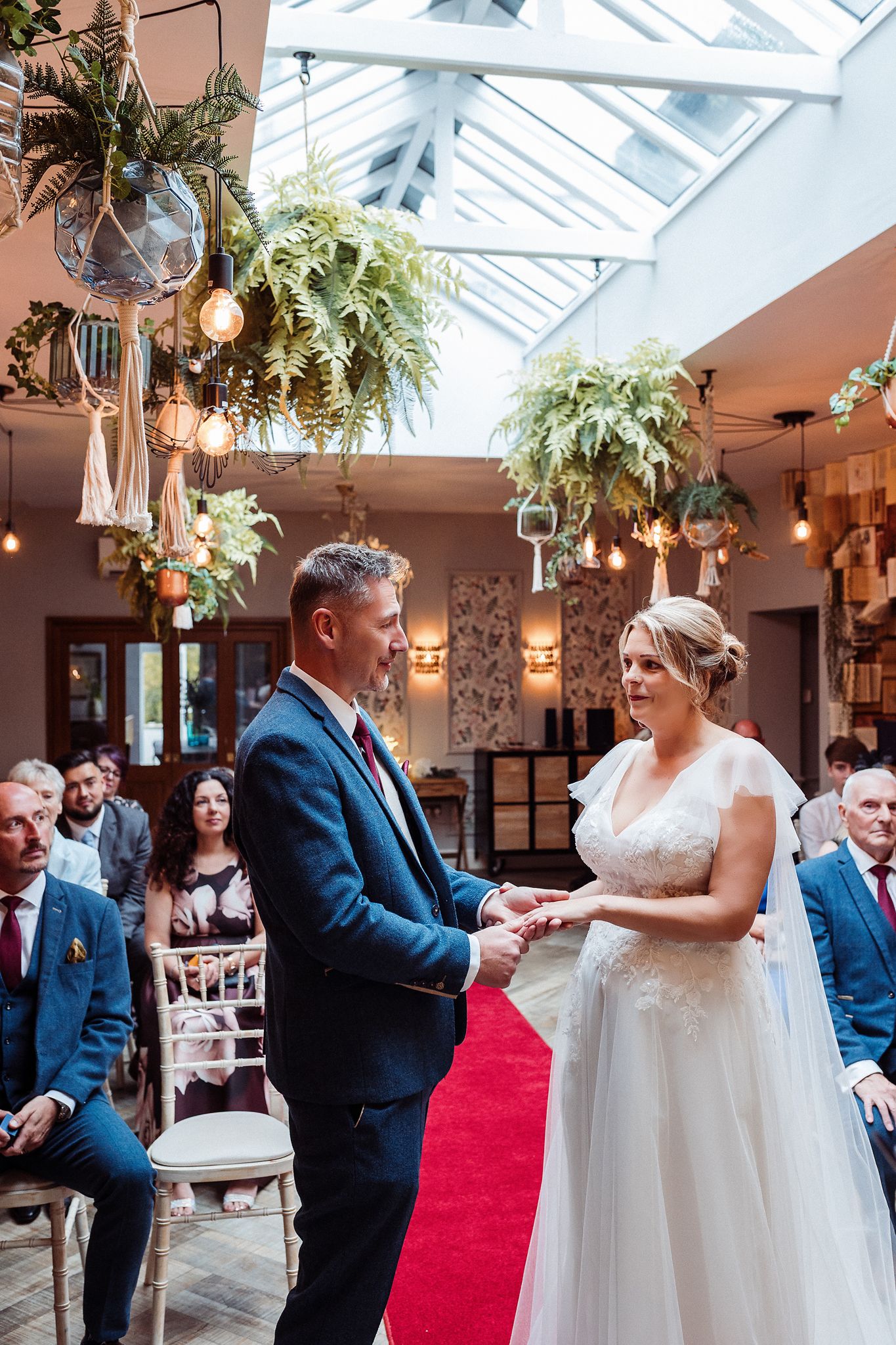 A couple shares their first dance together in a sunlit conservatory with hanging plants and string lights overhead.