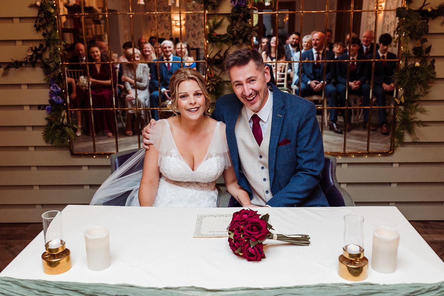 A couple shares a romantic moment at their wedding reception table decorated with deep red floral arrangements.