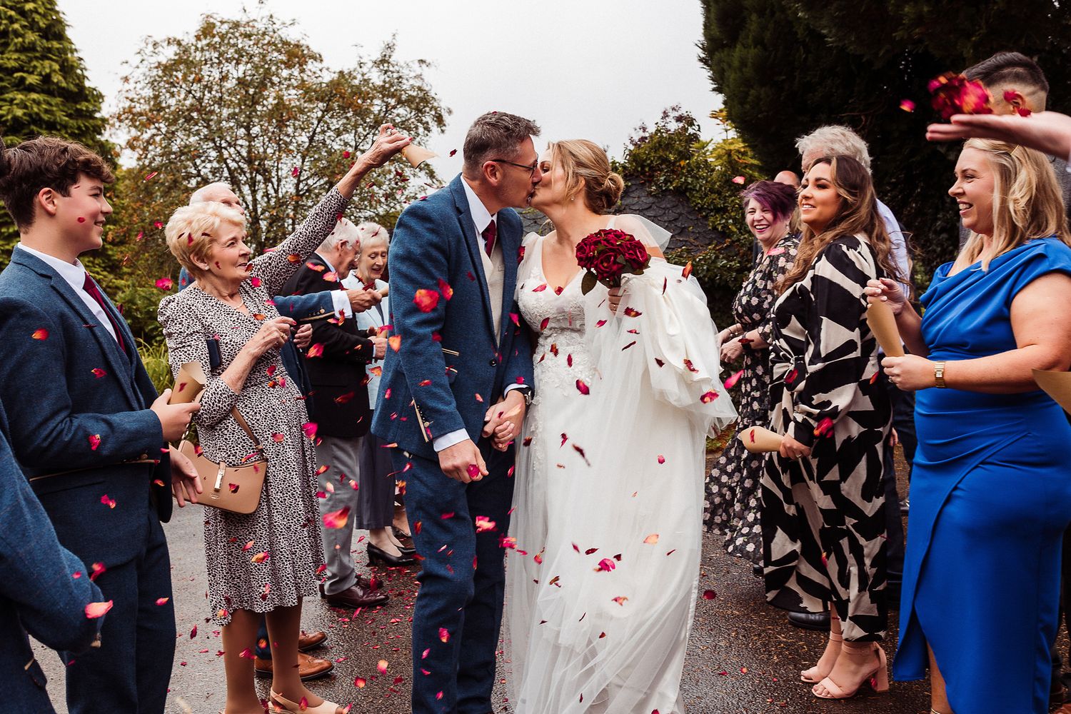 Wedding guests shower newlyweds with red and white confetti during outdoor celebration.