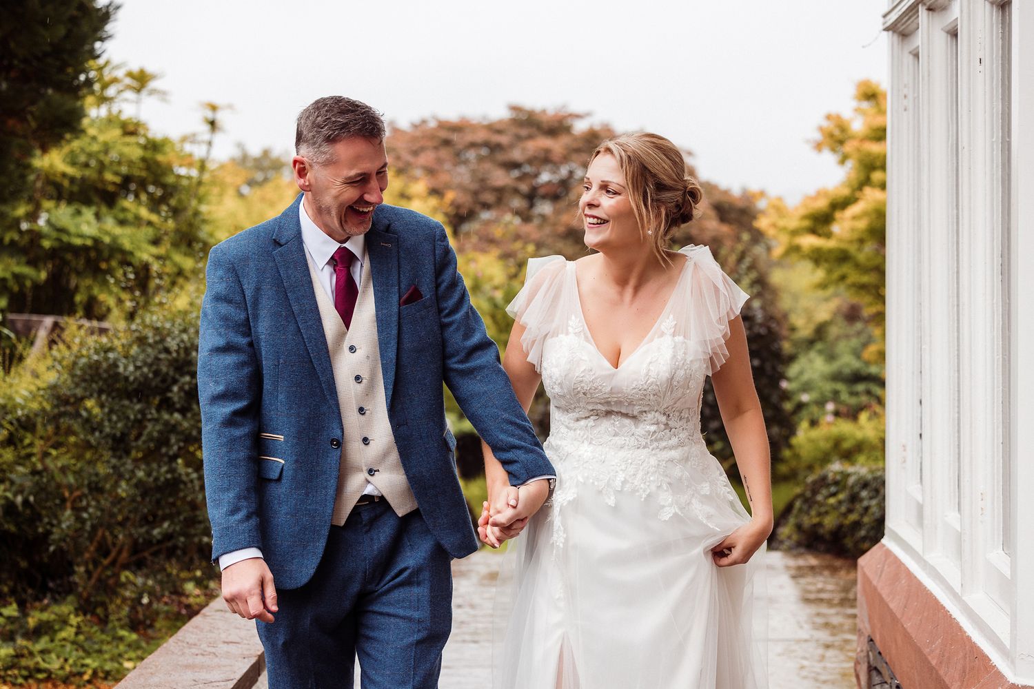A couple in wedding attire shares a joyful moment together on a white porch during an autumn day.