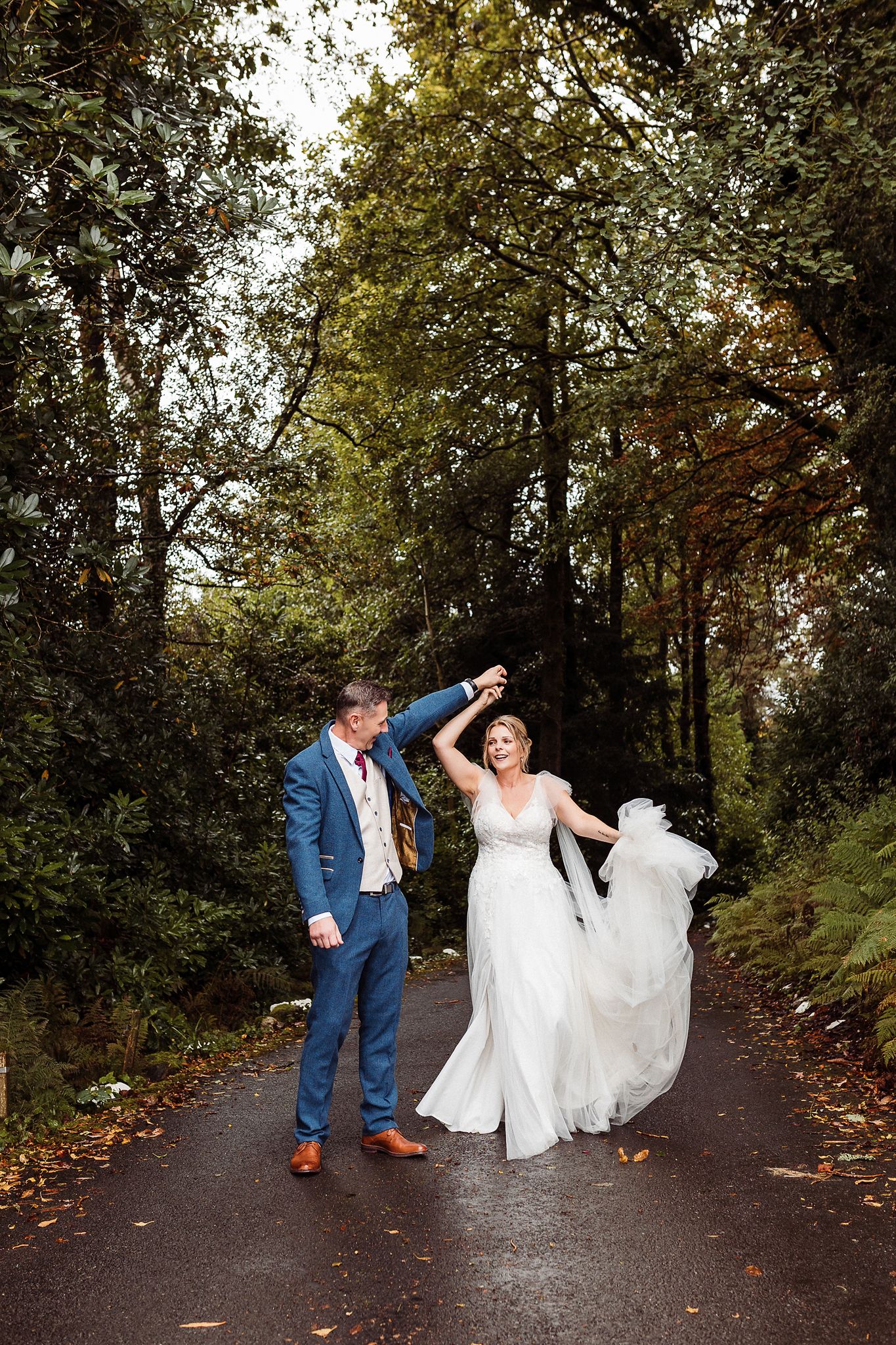 Playful couple dancing and twirling in a romantic autumn forest path covered with fallen leaves.