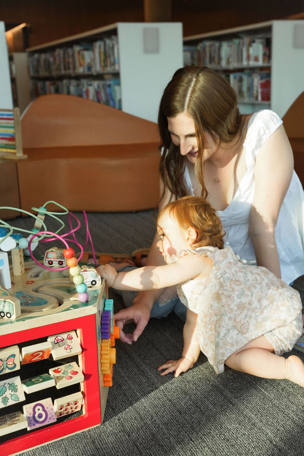 Children playing with educational toys and learning materials on a gray carpet in a library setting.