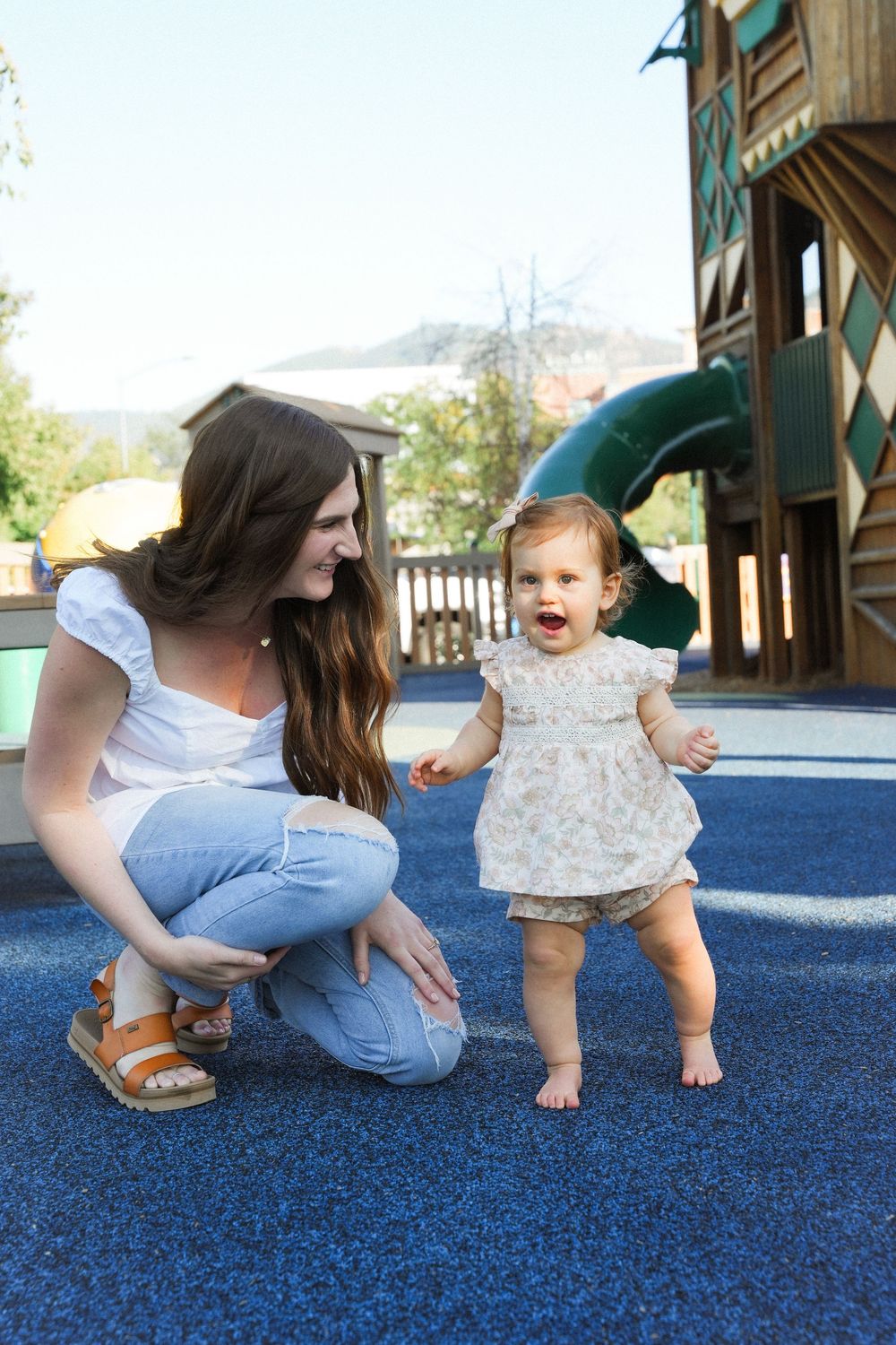 A sequence of photos showing a parent helping a baby learn to crawl on blue rubber playground flooring.