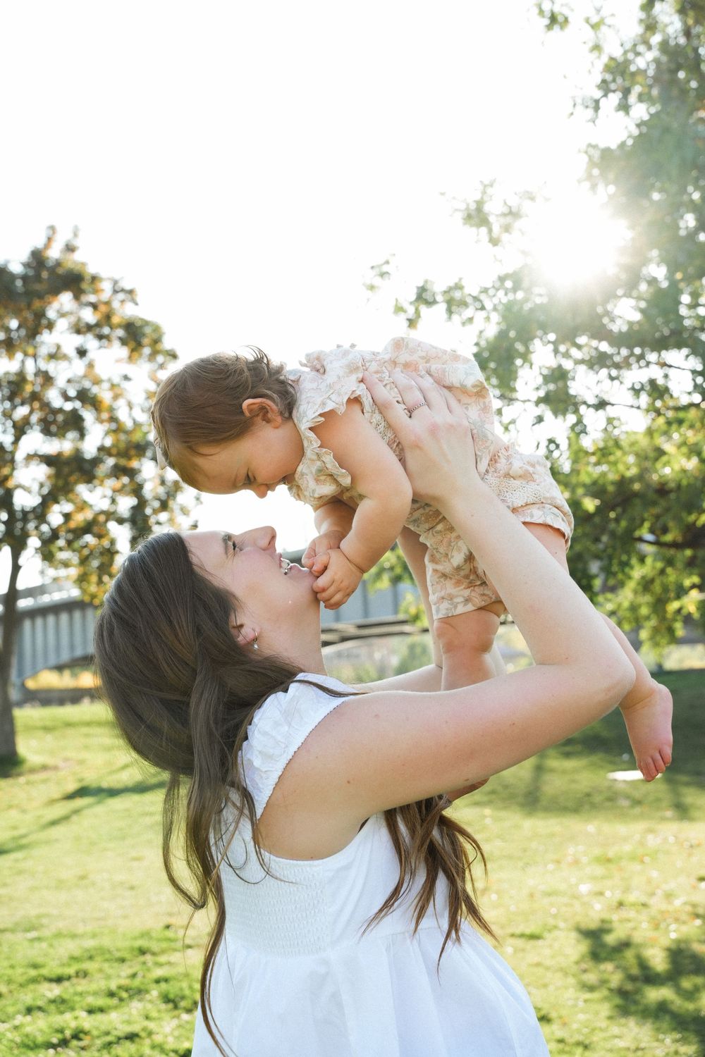 Parent and child playing together outdoors in a sunlit grassy field on a warm day.