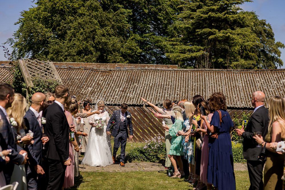 Wedding celebration panorama showing guests gathered on lawn near historic stone building.