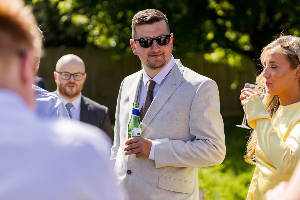 Wedding guests enjoying drinks and conversation in bright summer sunshine.