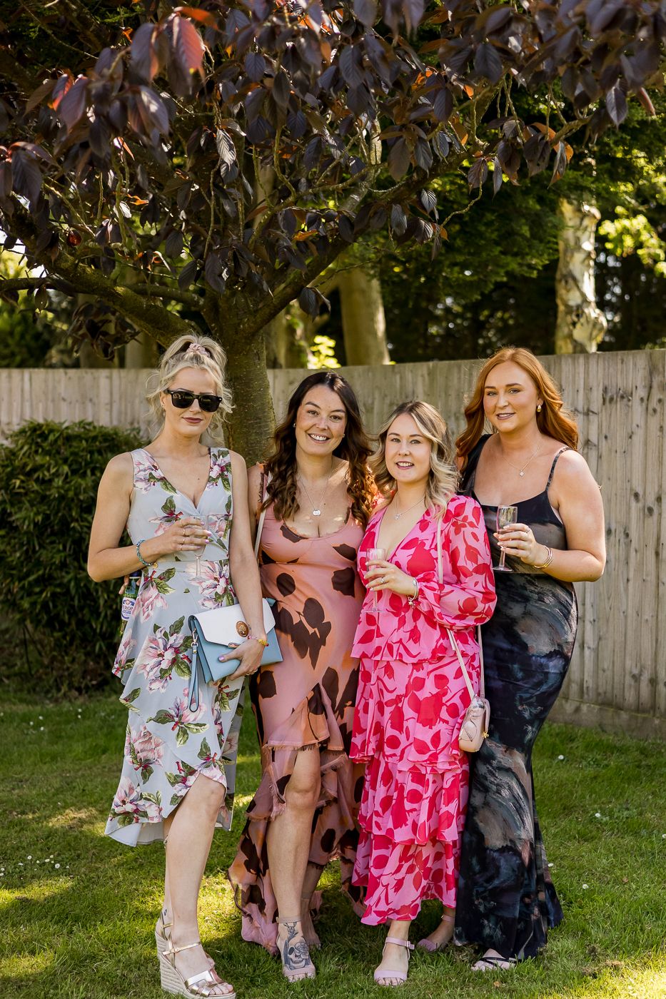 Friends in floral summer dresses relax on the lawn during a garden party.