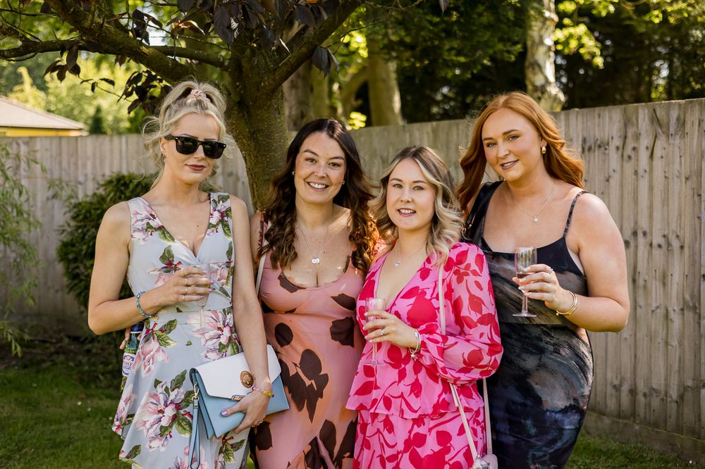 Wedding guests in colorful summer dresses socialize at an outdoor reception.