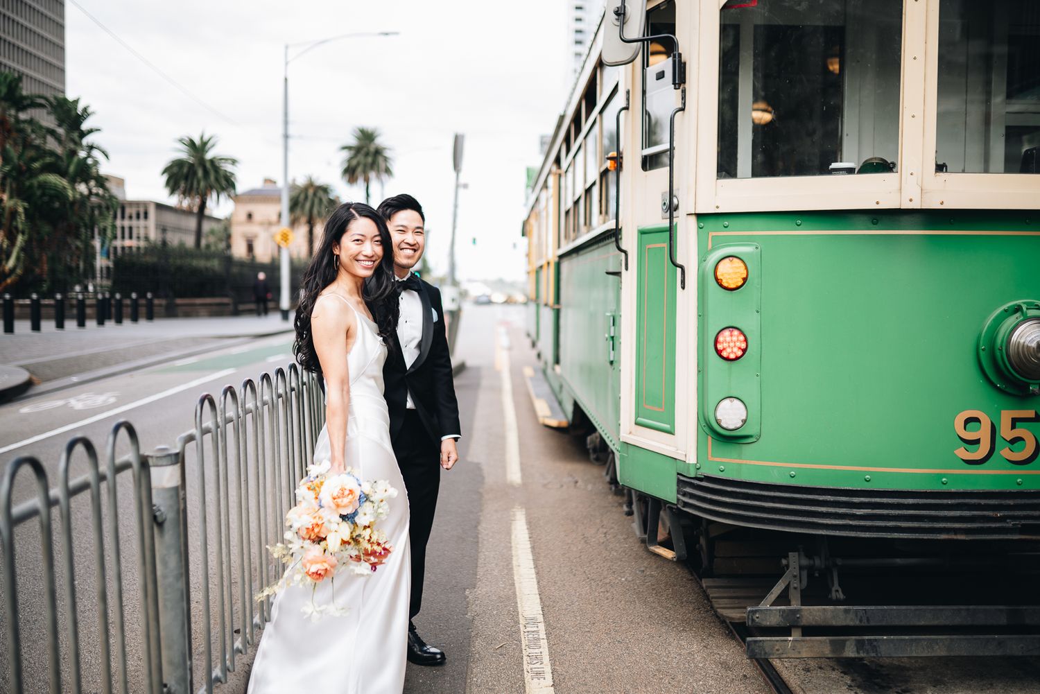 A couple poses for romantic wedding photos with a vintage green tram in Melbourne taken by Melbourne couples photographer.