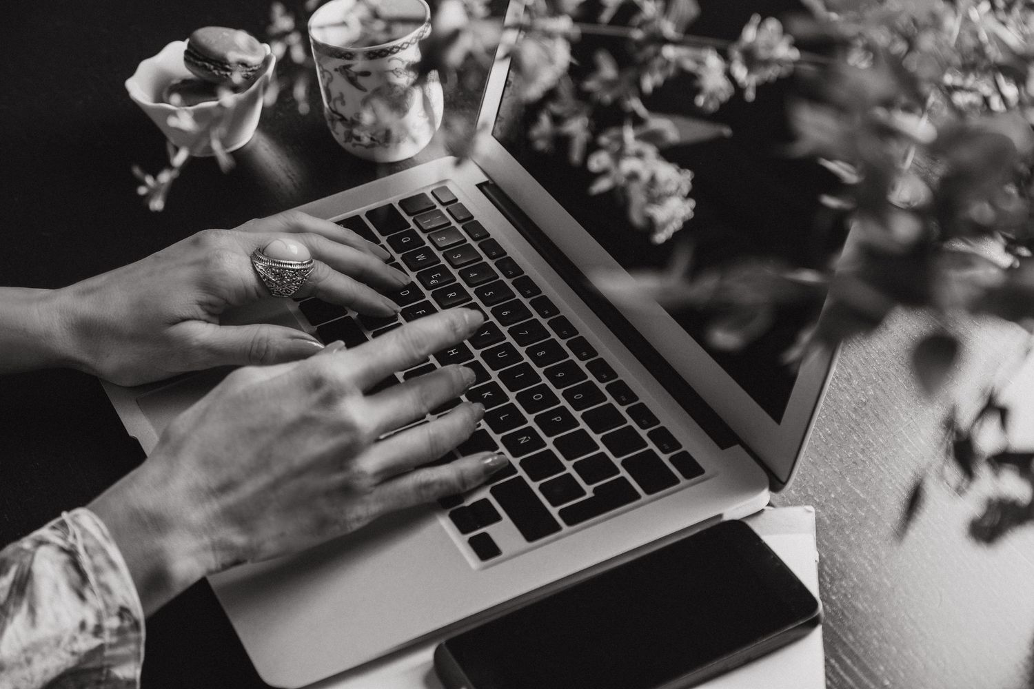 Wedding photographer at work, responding to client inquiries. Black and white detail shot with a laptop and flowers.