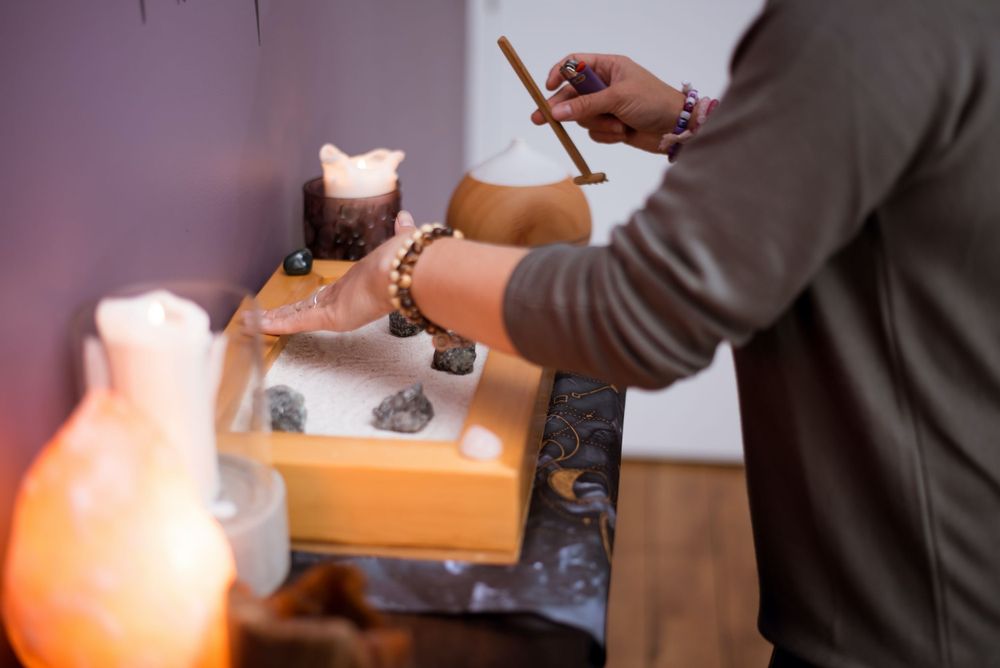Hands arranging crystals in a wooden box with lit candles nearby.
