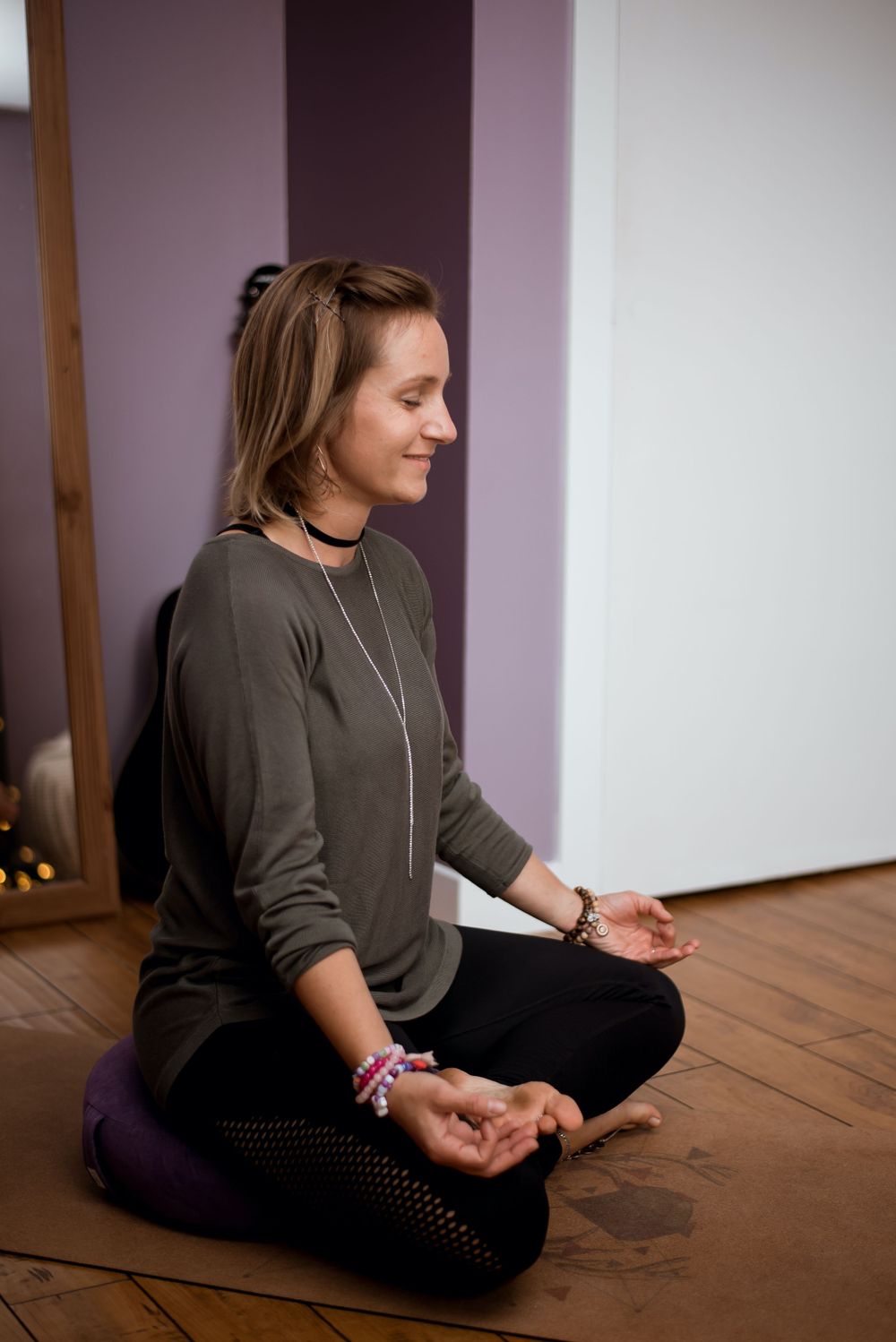 Side view of person in meditation pose wearing brown sweater against purple striped wall.