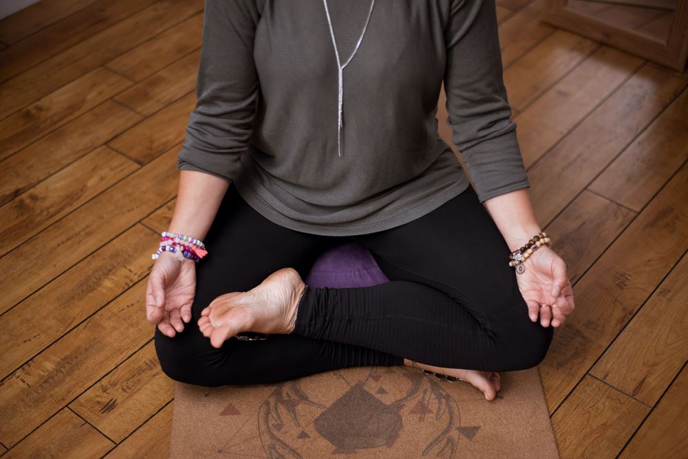 Peaceful meditation pose on wooden floor showing brown sweater and black pants.