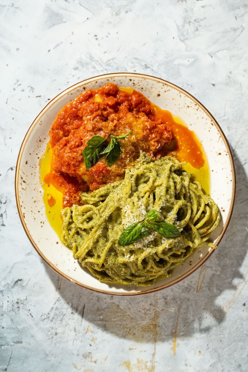 Half pesto pasta and half marinara sauce dish garnished with fresh basil on a white surface. Mtlshutter photography