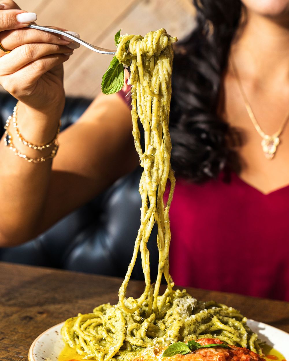 A plate of fresh pesto pasta with herbs being lifted by a fork against a warm background. Mtlshutter photography