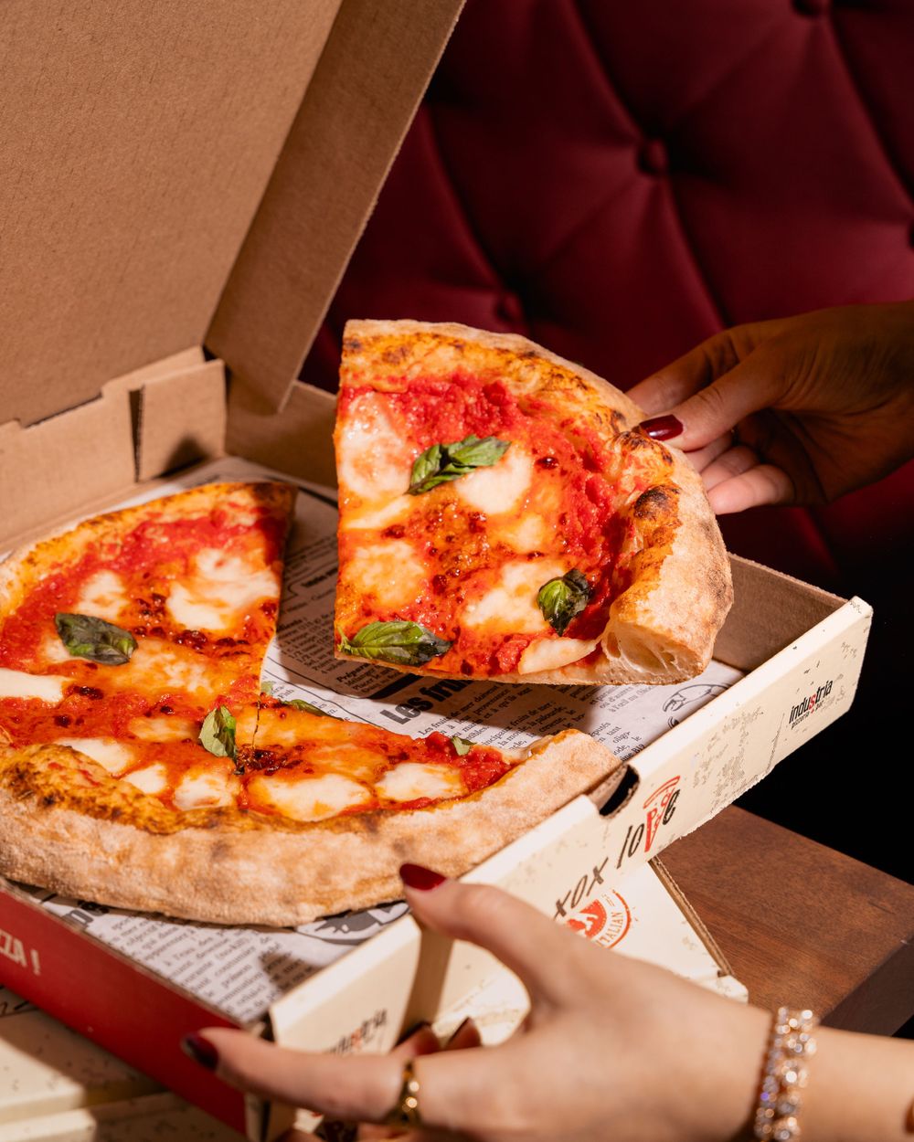 Hands reaching for slices of Margherita pizza with fresh mozzarella and basil from an open delivery box.