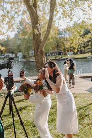 Wedding party with cameras and bouquets posing by the lake on an autumn day.