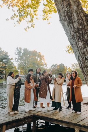 Group of friends laughing together on a wooden dock during autumn with colorful fall foliage in the background.