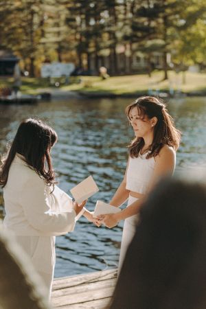 Intimate wedding ceremony taking place on a wooden dock with water and trees in the background.