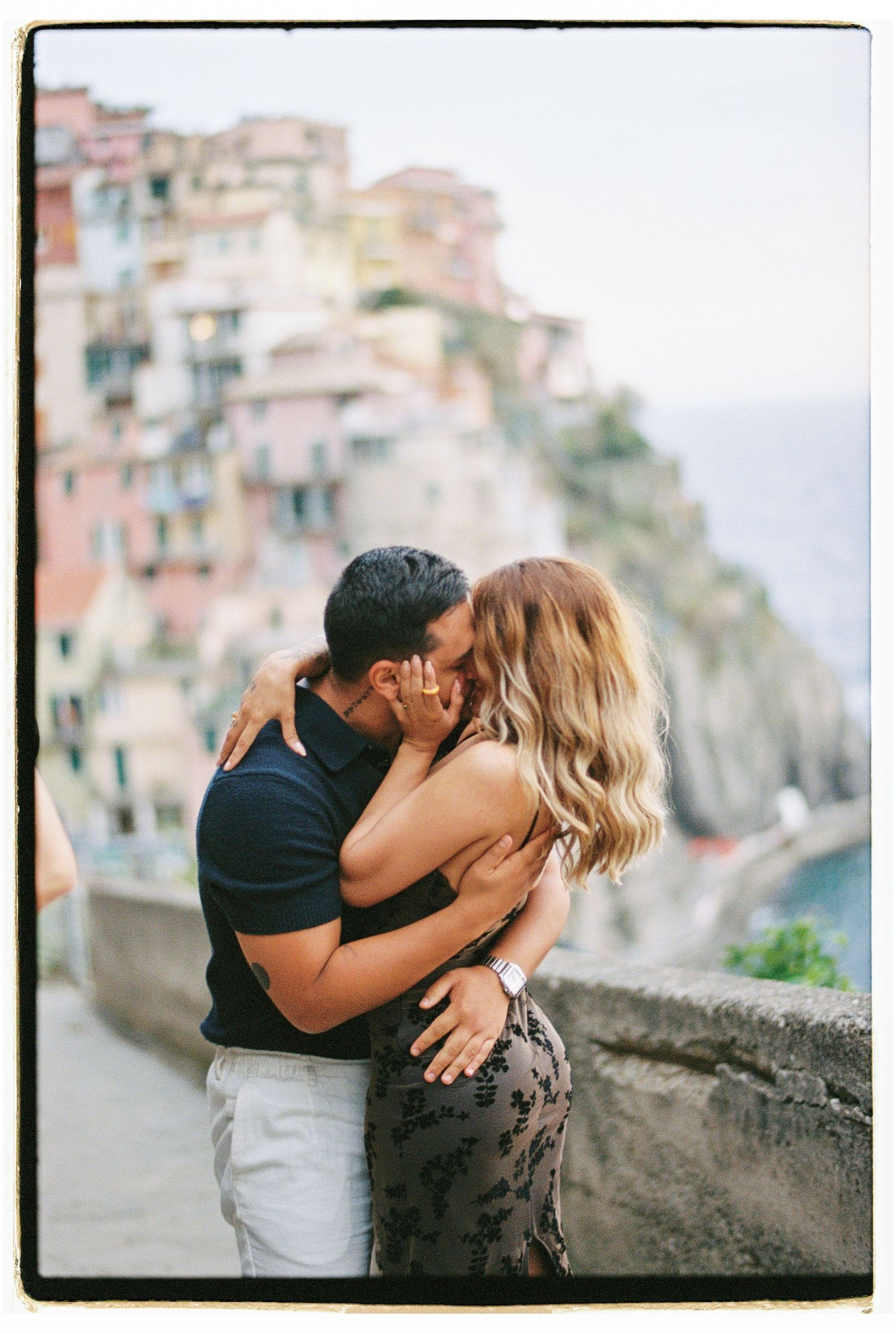 Romantic couple kissing against colorful Cinque Terre village backdrop in Italy.