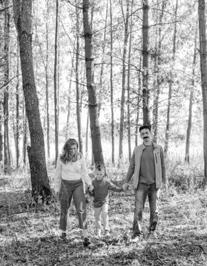 Family walking together through sunlit forest in black and white.