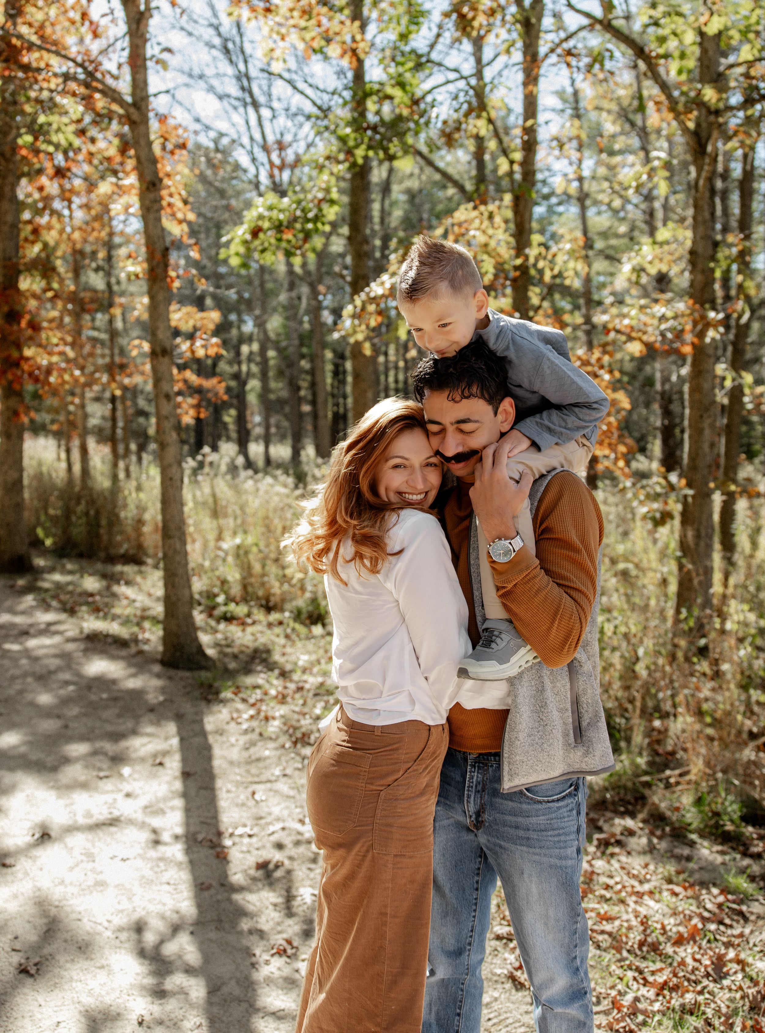Lifestyle family photographer capturing joyful parents holding toddler son on shoulders in autumn forest