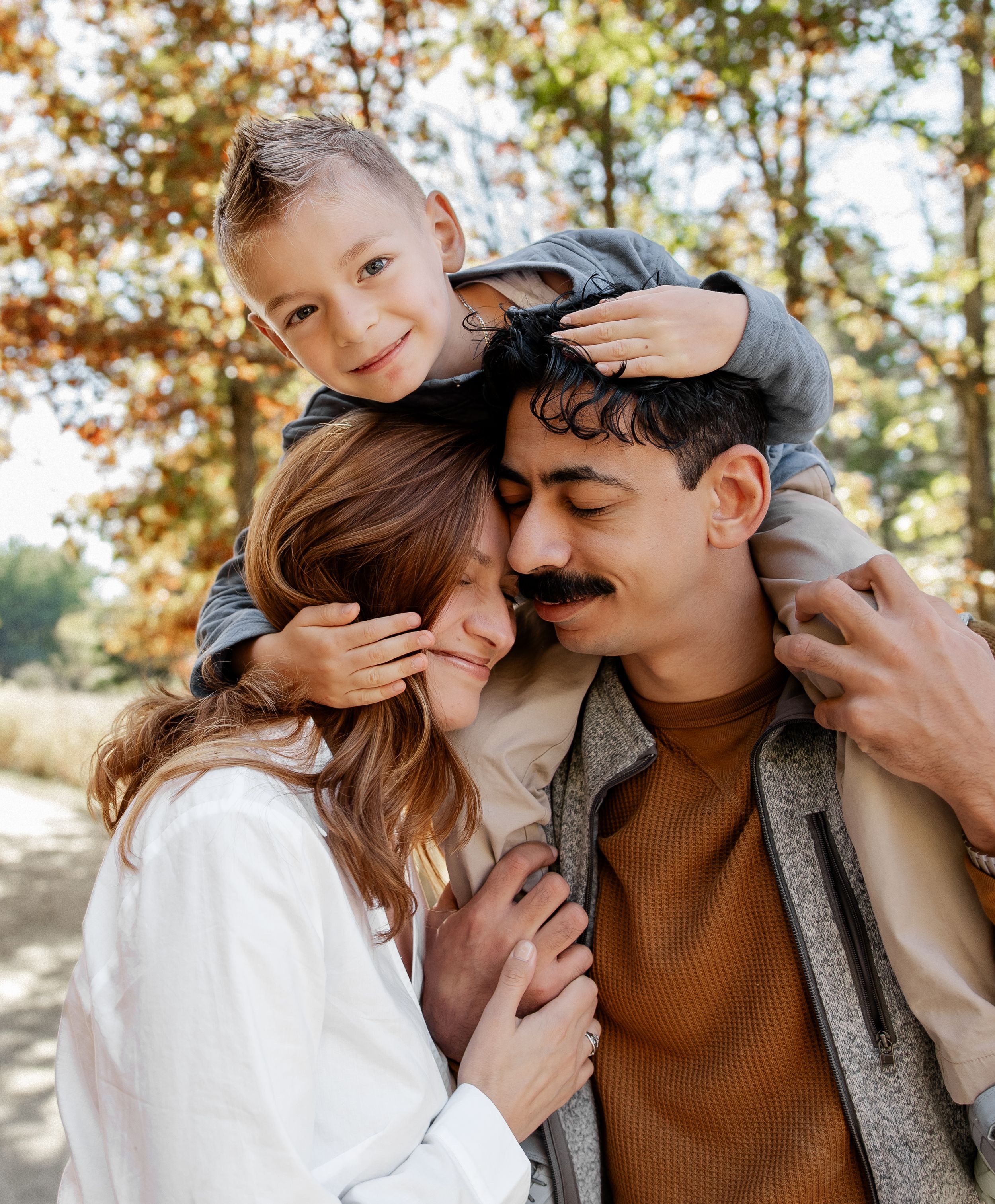 Lifestyle family Chicago photographer capturing loving parents cuddling toddler son on shoulders in sunlit autumn forest