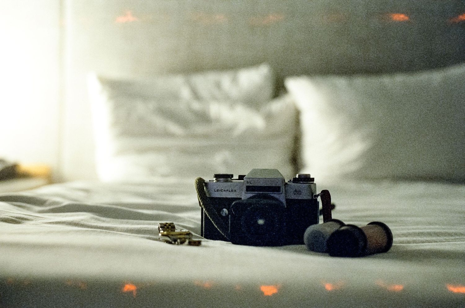 Film camera and accessories arranged on white bedsheets in natural light.